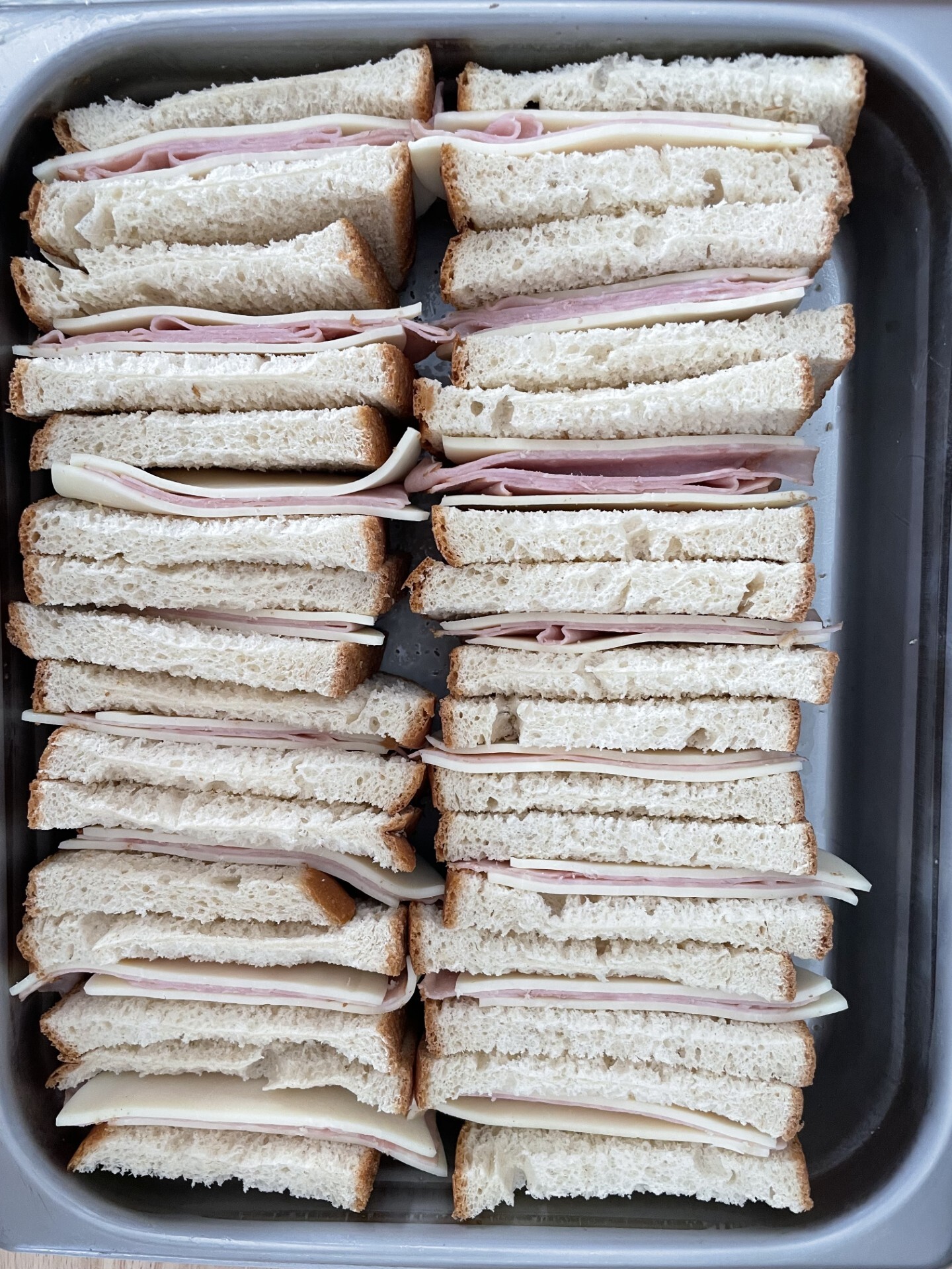 Halved ham and cheese sandwiches standing on their cut sides in a half hotel pan